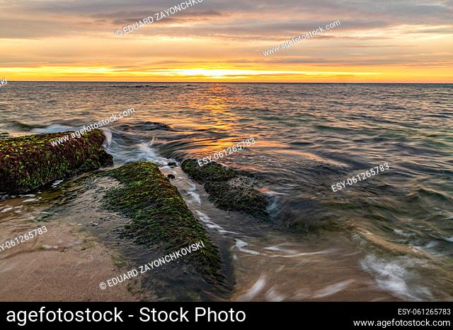 Seascape view of a calm sea with rocks with moss. Beauty sky with clouds at the horizon