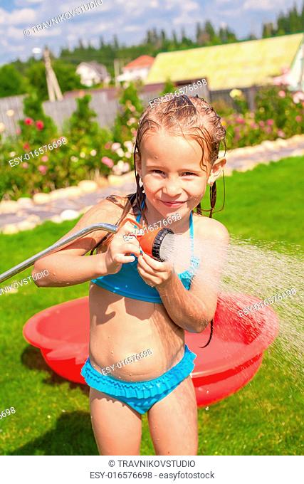Happy adorable little girl smiling and pouring water from a hose