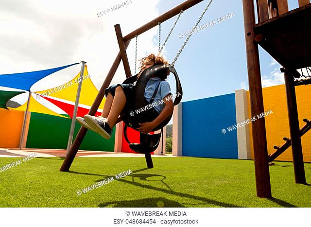 Schoolgirl playing in a swing swing in the school playground