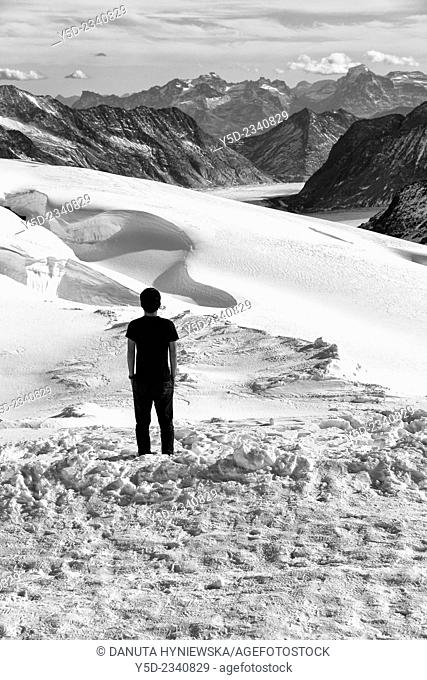 Single young man in T-shirt looking at distant view of mountains and Aletsch glacier, Jungfraujoch, Swiss Alps, Switzerland