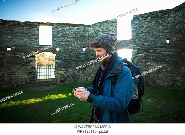 Male hiker using mobile phone in old ruin at countryside
