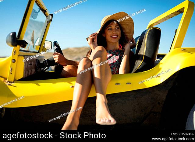 Happy caucasian woman sitting in beach buggy by the sea wearing straw hat