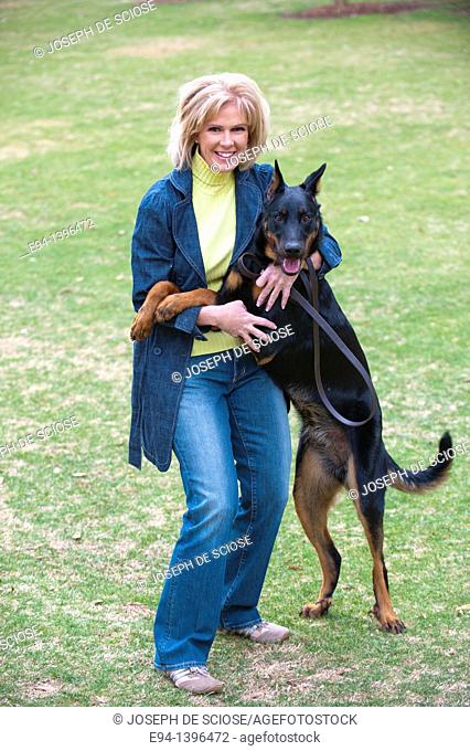 Fifty year old blond woman playing with a Doberman Pinscher in a park