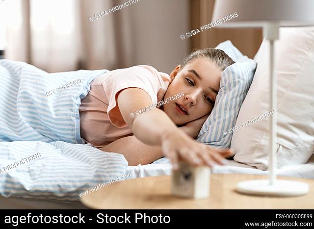 sleepy girl with alarm clock awaking in bed