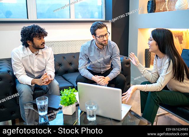 Young company worker sitting with her male colleagues around the coffee table during the meeting