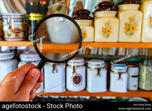 A point of view perspective of a man holding a magnification lens inside the kitchen storage cupboard, with blurred airtight containers and copy-space