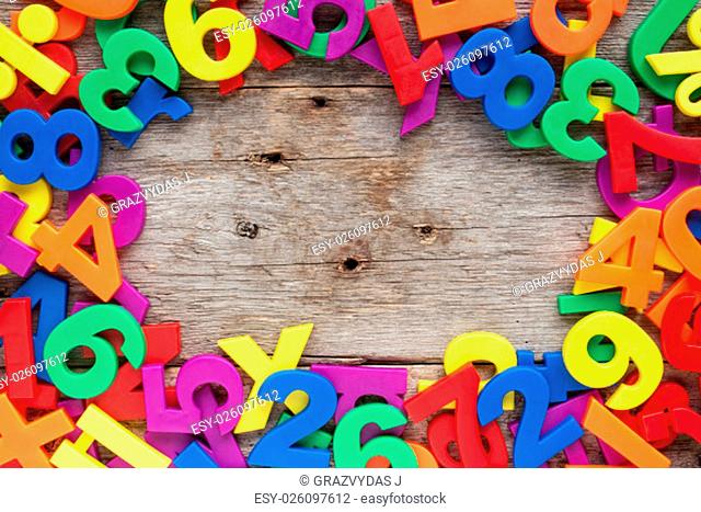 Top border of colorful toy magnetic letters and numbers over a wooden background