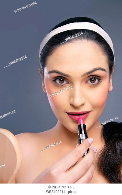 Portrait of a beautiful female applying lipstick over colored background