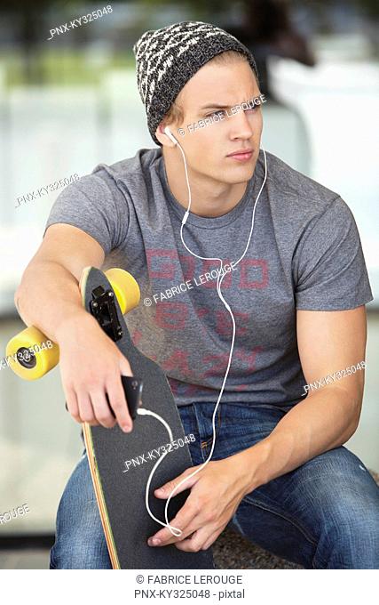 Man holding a skateboard and listening to music on a mobile phone