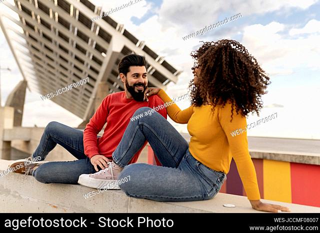 Happy couple sitting on wall in front of solar panels
