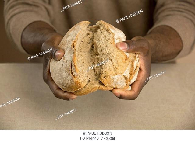 Midsection of man breaking bread loaf at table