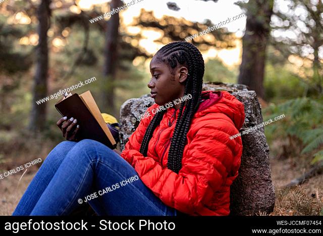 Young woman with braided hair reading book in forest