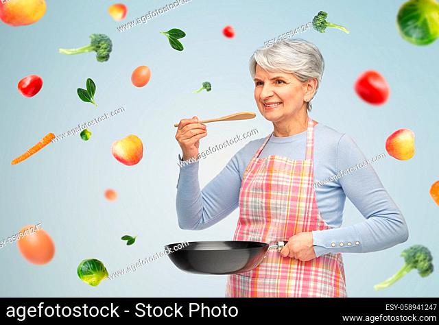 smiling senior woman in apron with frying pan