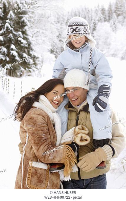 Family in snow-covered forest, man carrying boy (6-9) on shoulder, portrait