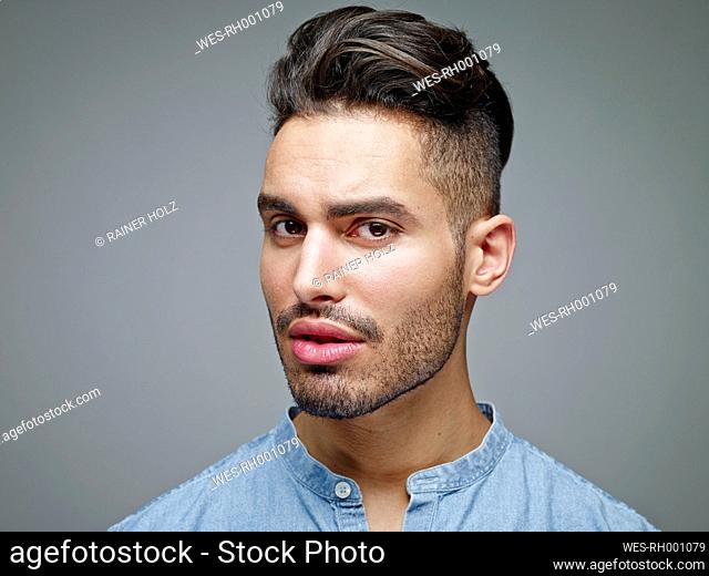 Portrait of sceptical looking young man in front of grey background