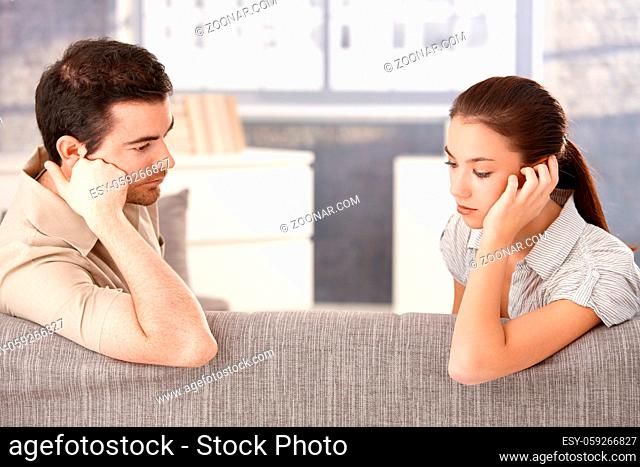 Young couple sitting on sofa at home sadly after quarrelling