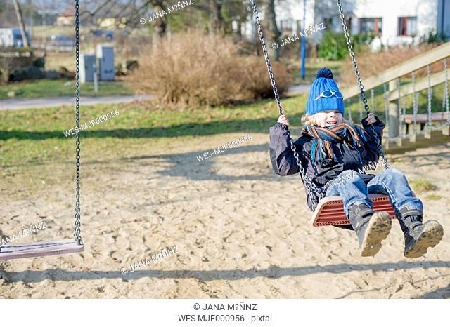 Germany, Mecklenburg-Western Pomerania, Ruegen, little boy swinging at playground
