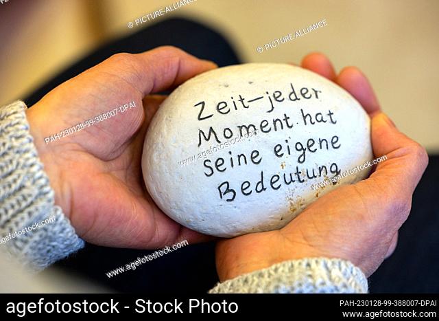 PRODUCTION - 26 January 2023, Thuringia, Weimar: A grief counselor holds a stone with the inscription ""Time - every moment has its own meaning""