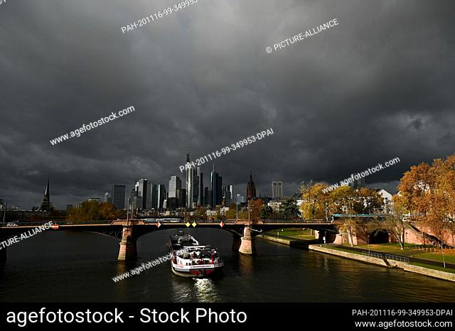 16 November 2020, Hessen, Frankfurt/Main: While dark rain clouds pass over the city and the sun shines briefly on the Ignatz-Bubis-Bridge