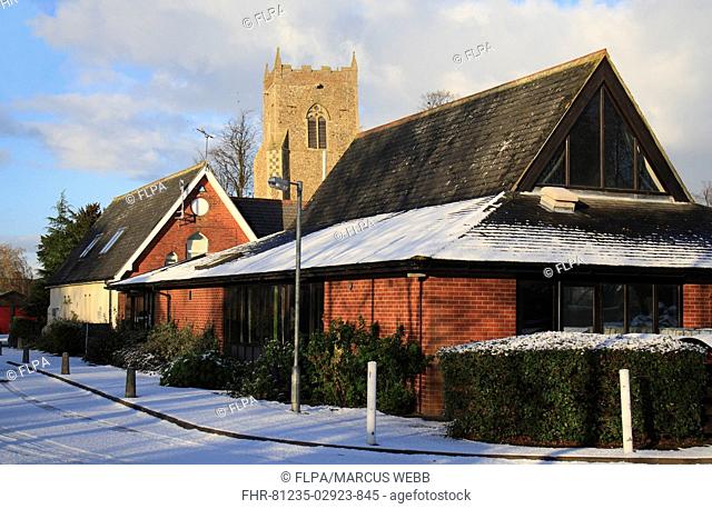 Village daycare centre, primary school and church tower in snow, St Mary's Church, Bacton, Suffolk, England, november