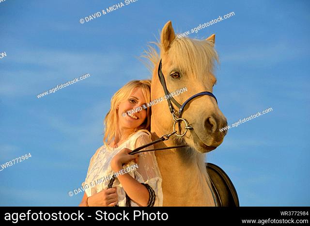 Smiling woman in white dress with horse under blue sky