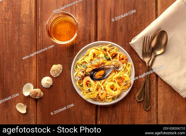 Seafood pasta. Tagliolini with mussels, shrimps, clams and squid rings, with a glass of wine, shells, a fork, and a spoon
