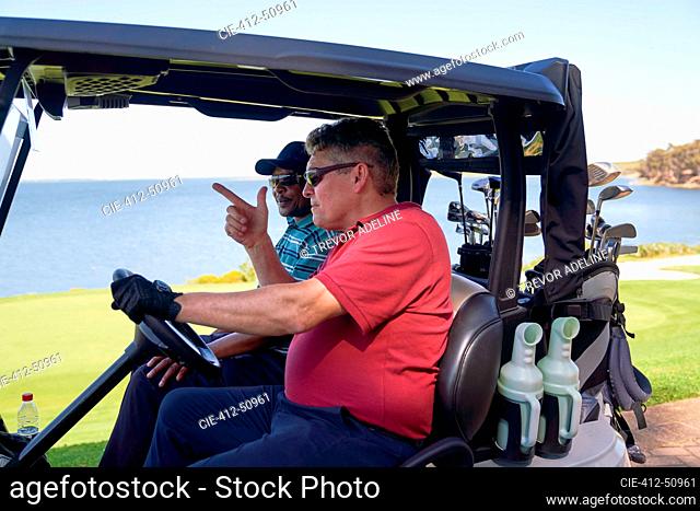 Male golfers driving golf cart on lakeside golf course