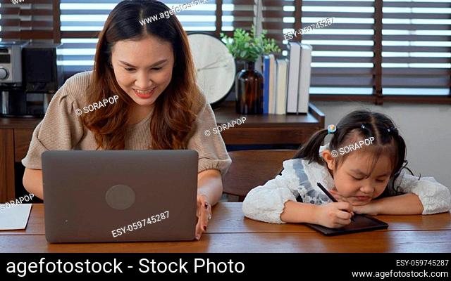 Asian young mother working with laptop computer at home and help daughter doing homework, Single mom freelancer work from home and helping his girl kid teaching...