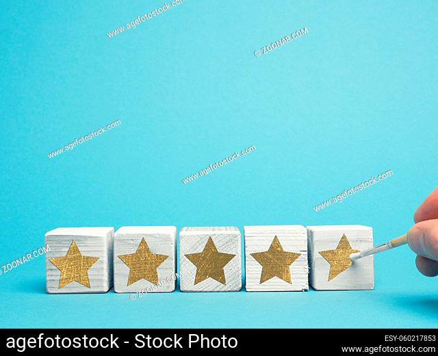 5 stars rating concept, man painting golden stars with brush on wooden cubes