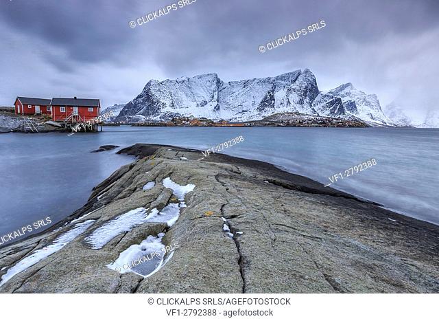 Typical red houses in the Hamnøy landscape with its cold sea and snow capped peaks. Lofoten Islands Norway Europe