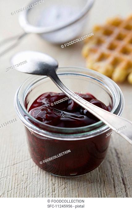 Cherry jam in a glass, waffles and icing sugar