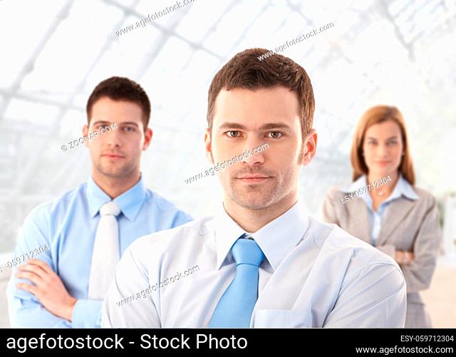 Team of young businesspeople standing arms crossed in office lobby