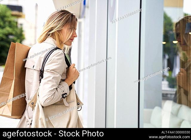 Side view shot of woman carrying bags while window shopping