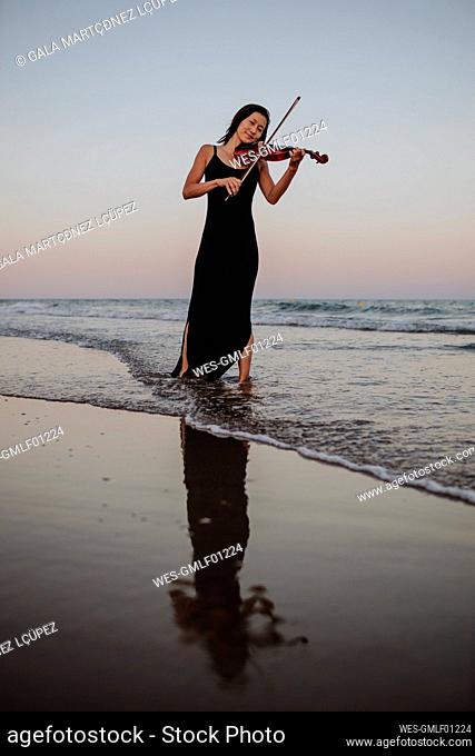 Woman playing violin standing in sea at sunset