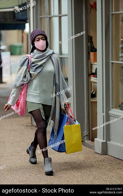 Young woman in face mask with shopping bags on sidewalk