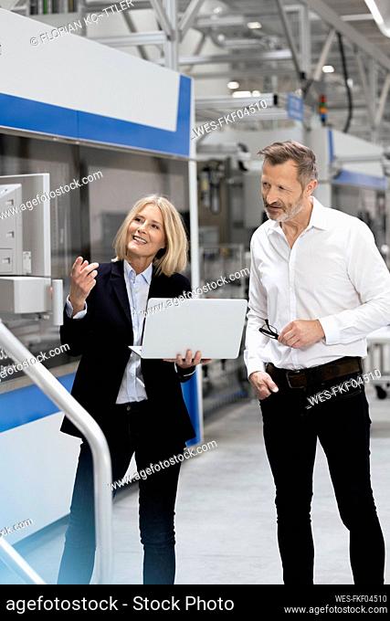 Mature businesswoman with laptop explaining to male professional in industry