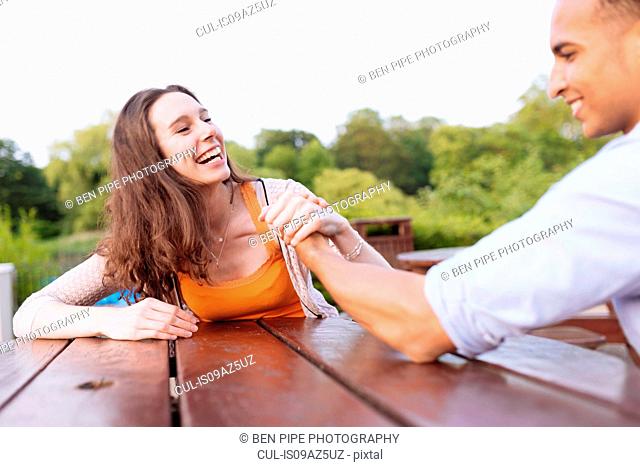 Young couple arm wrestling on picnic bench laughing