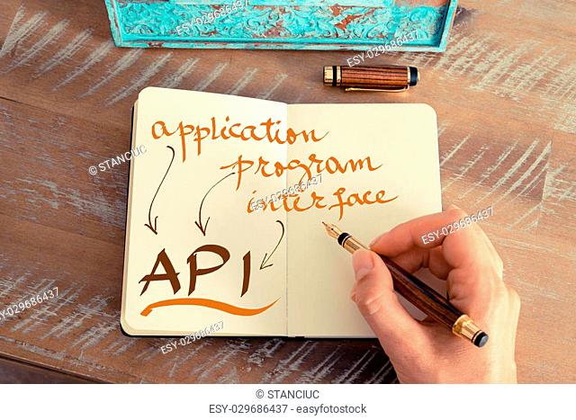 Retro effect and toned image of a woman hand writing a note with a fountain pen on a notebook. Handwritten text API APPLICATION PROGRAM INTERFACE
