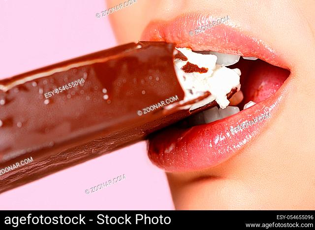 face of a beautiful young girl close-up. she bites the ice cream with her mouth. on a pink isolated background