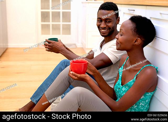 African american couple sitting on floor in kitchen holding mugs