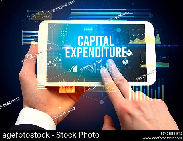 Close-up of hands holding tablet with CAPITAL EXPENDITURE inscription, modern business concept