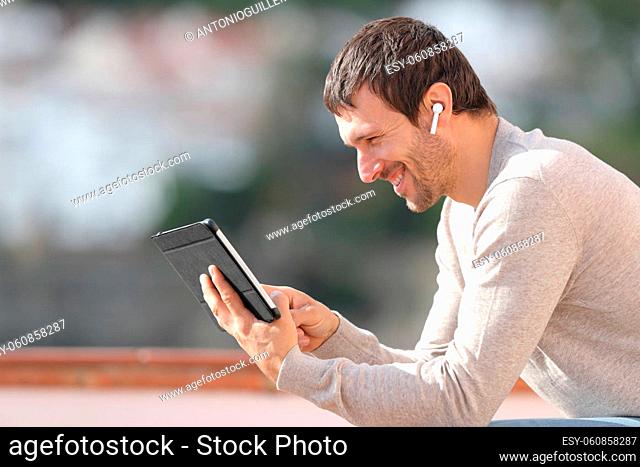 Profile of happy man watching media with tablet and earbuds