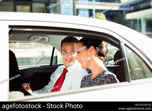 Businessman and businesswoman talking in back seat of car