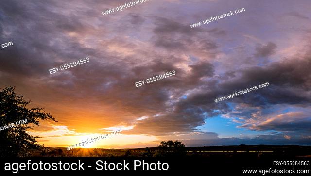 Spring meadow after rain, cloudy evening pre sunset sky with rainbow, rural hills and fields in far panorama view. Natural seasonal, weather, climate