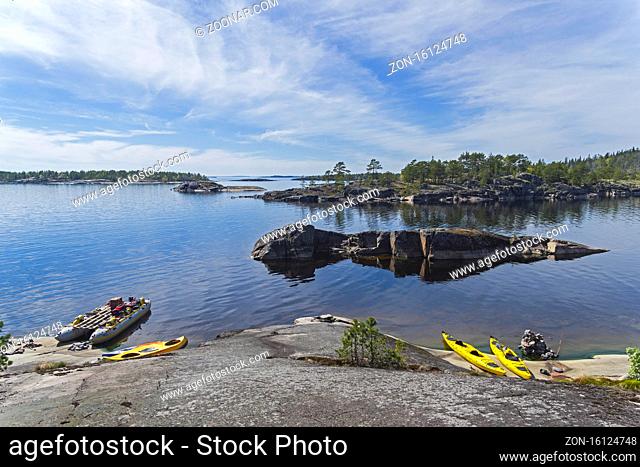 Tourist catamaran and kayaks at the granite shore. Ladoga skerries, Karelia, Russia. Sunny day in early June