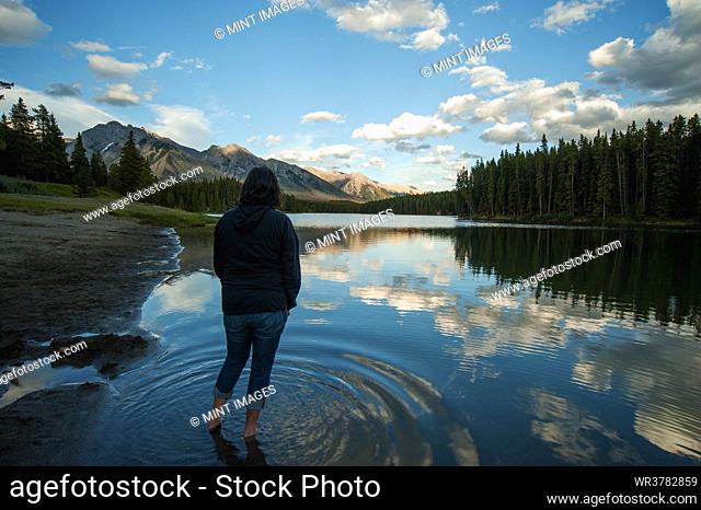 Woman standing in shallow water of Johnson Lake in Banff National Park looking at mountains and rural scene