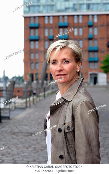 Blond haired executive woman, turning her head around to the camera, seen from side, with office building made of red bricks