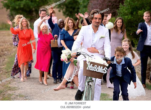 Wedding guests waving off newlyweds on bicycles