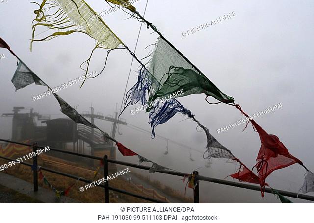 30 October 2019, Bavaria, Oberstdorf: A chairlift stands behind Tibetan prayer flags on the foghorn in the fog and rain. Photo: Karl-Josef Hildenbrand/dpa