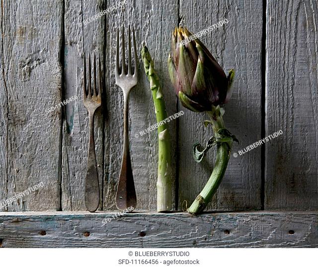Artichoke, asparagus and rusty forks against a rustic wooden wall